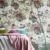 Summer Tropical Bloom Collection wallpaper depicting vibrant pink flowers and rich green leaves, creating a dynamic and lush backdrop for a cozy bedroom setting with colorful pillows.