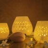 Jaali Blaze large candle holders in varying sizes, emitting a warm, patterned glow, set against a dusky backdrop with delicate floral embellishments