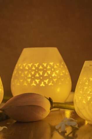 Jaali Blaze large candle holders in varying sizes, emitting a warm, patterned glow, set against a dusky backdrop with delicate floral embellishments
