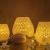 Jaali Blaze large candle holders in varying sizes, emitting a warm, patterned glow, set against a dusky backdrop with delicate floral embellishments