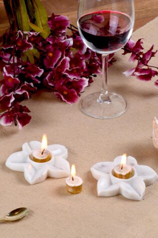 Delicate white marble 'Starlight' candle holders by Natural Handicrafts, with small tea candles lit, enhancing the floral ambiance on a textured tablecloth.