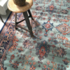 Oriental hand knotted rug with aquamarine blue, black, and rust colors under a metal chair.
