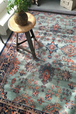 Oriental hand knotted rug with aquamarine blue, black, and rust colors under a metal chair.