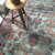 Oriental hand knotted rug with aquamarine blue, black, and rust colors under a metal chair.