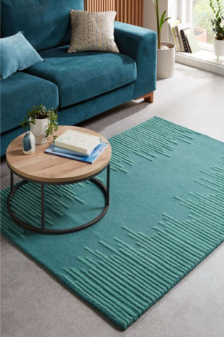 Teal blue geometric hand-tufted rug from the Signature Collection, made from 100% New Zealand wool, placed under a wooden coffee table.