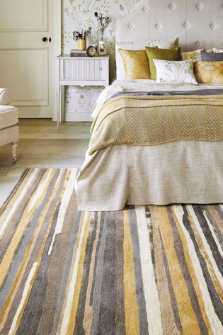 Hand-tufted rug with vibrant stripes of yellow, brown, black, and off-white, placed beside a cozy bed.