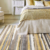 Hand-tufted rug with vibrant stripes of yellow, brown, black, and off-white, placed beside a cozy bed.