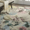 Hand-tufted floral rug with off-white, pinks, blues, greens, and browns, placed beside a cozy chair in a stylish living room.