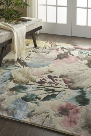 Hand-tufted floral rug with off-white, pinks, blues, greens, and browns, placed beside a cozy chair in a stylish living room.